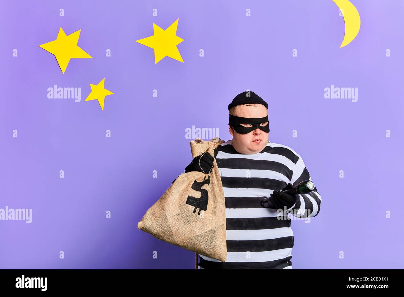 serious fat thief carrying a big bag, dressed in striped clothes, mask and  gloves holding a torch at night. close up photo. isolated blue background  Stock Photo - Alamy