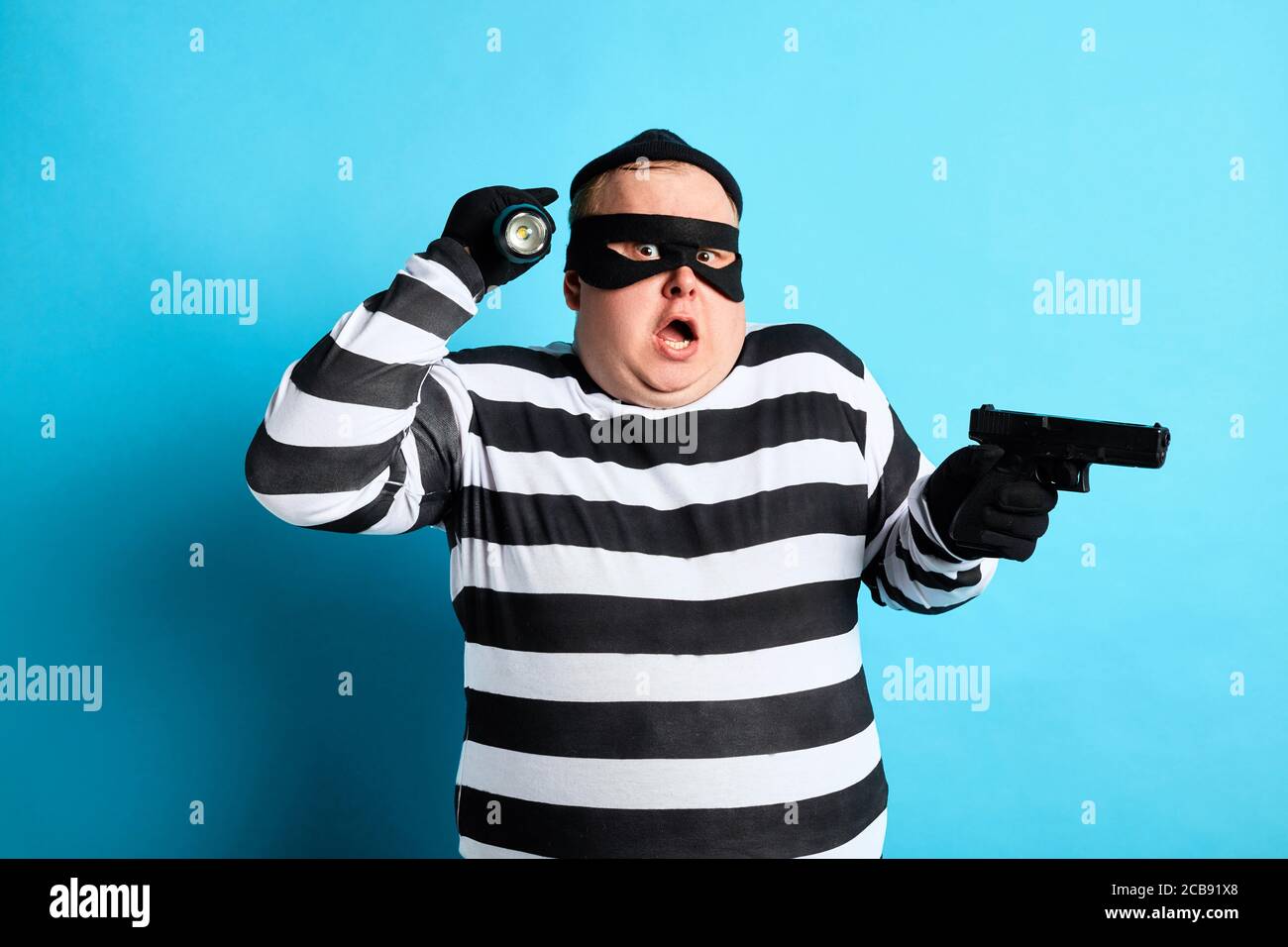 puzzled plump thief holding a gun on a blue background. isolated blue background. studio shot Stock Photo