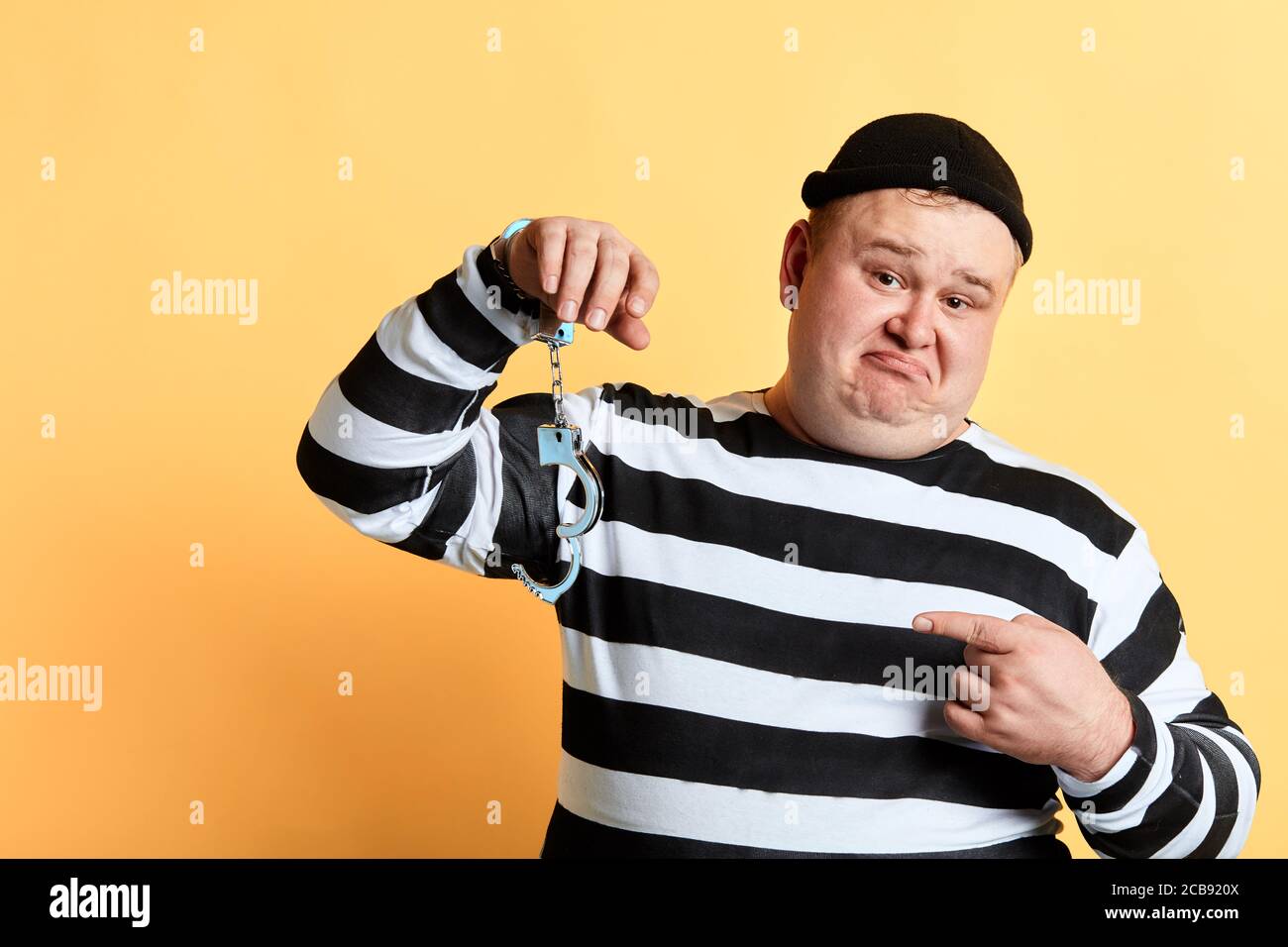 sad unhappy fat man pointing to unlocked handcuffs hanging on his hand. isolated yellow background, studio shot.criminal has broken cuff Stock Photo