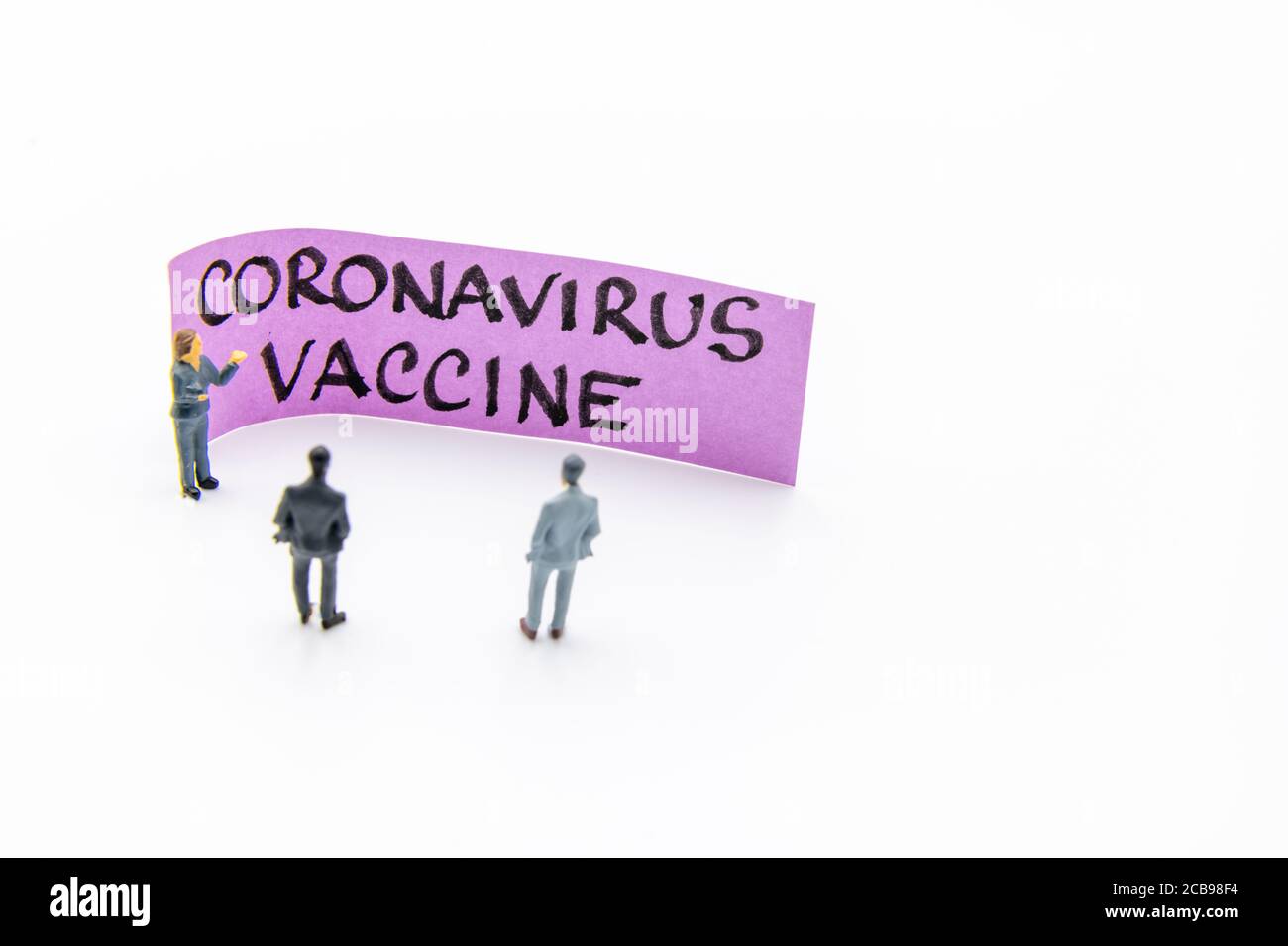 Presentation meeting with miniature figurines posed as business people standing in front of post-it note with Coronavirus Vaccine handwritten message Stock Photo