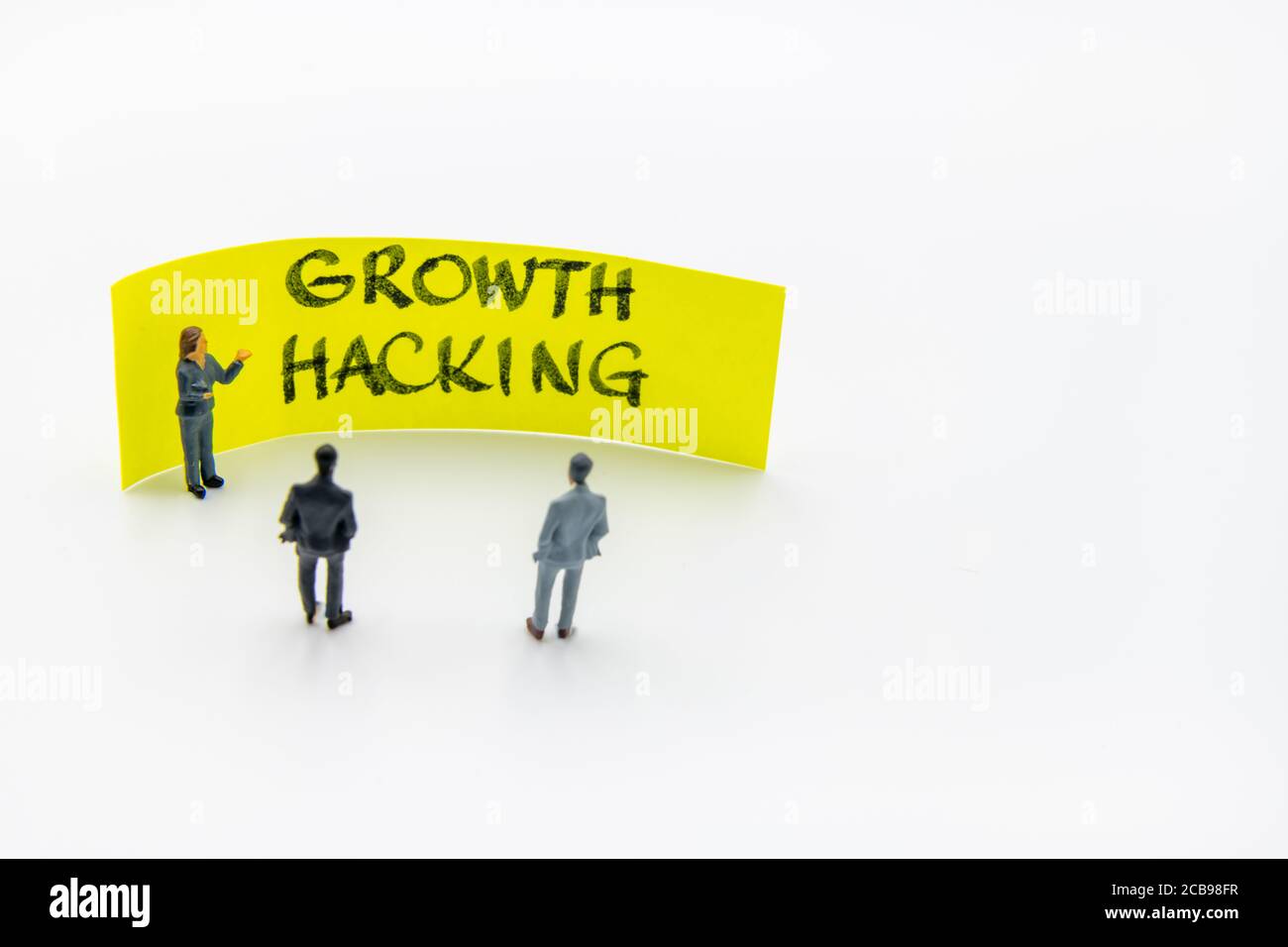 Presentation meeting with miniature figurines posed as business people standing in front of post-it note with Growth Hacking handwritten message in ba Stock Photo