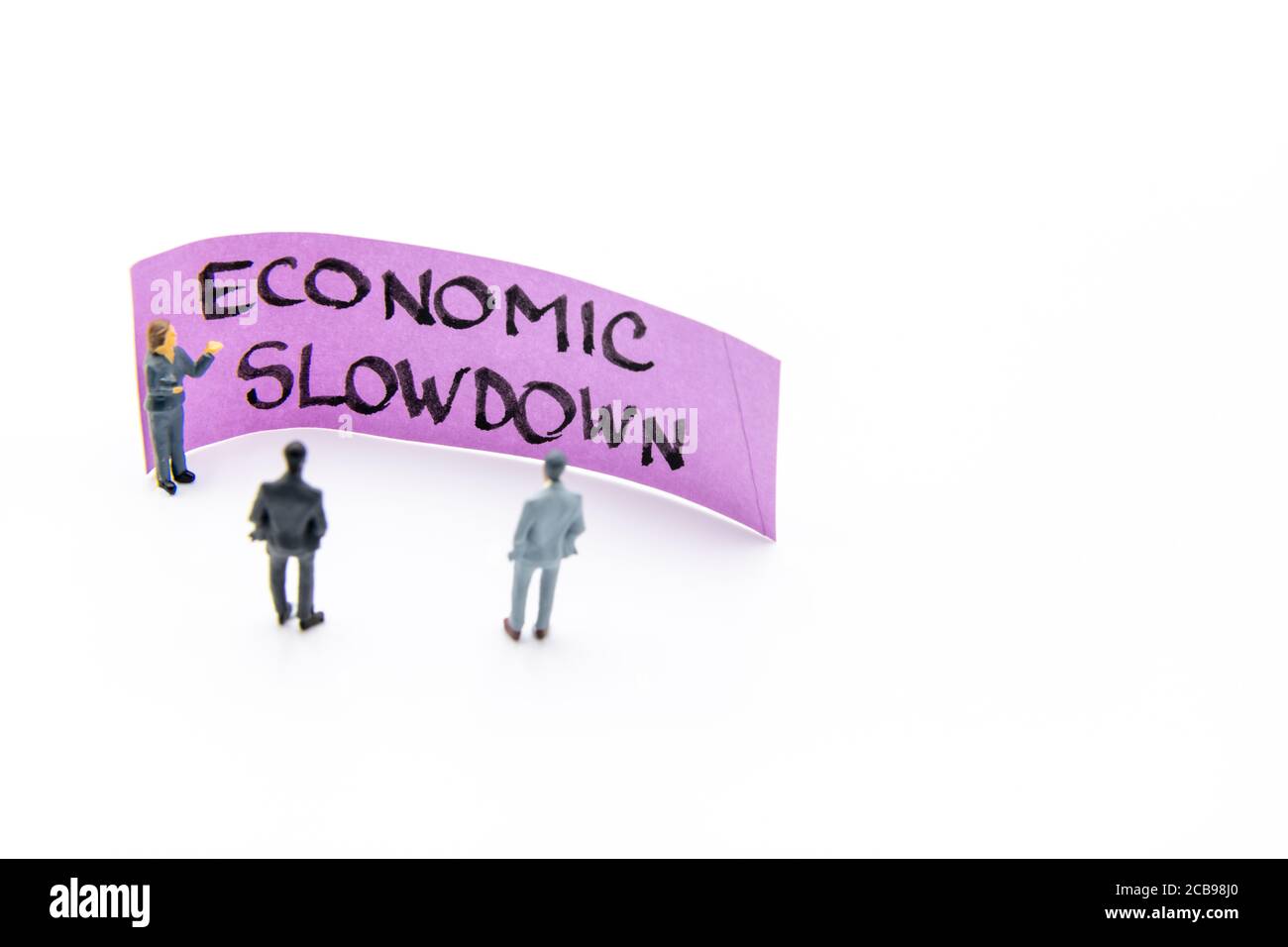 Presentation meeting with miniature figurines posed as business people standing in front of post-it note with Economic Slowdown handwritten message in Stock Photo