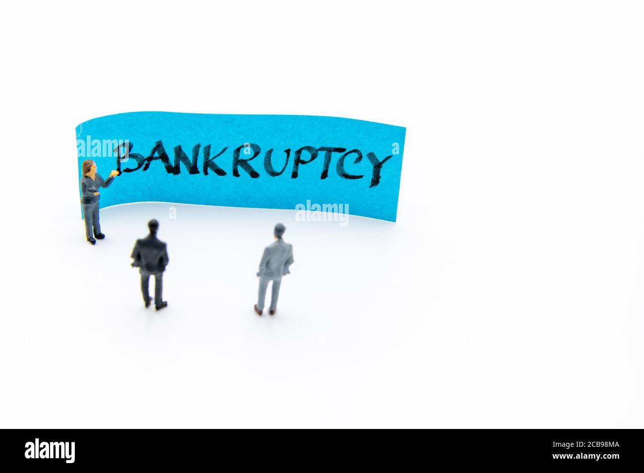 Presentation meeting with miniature figurines posed as business people standing in front of post-it note with Bankruptcy handwritten message in backgr Stock Photo