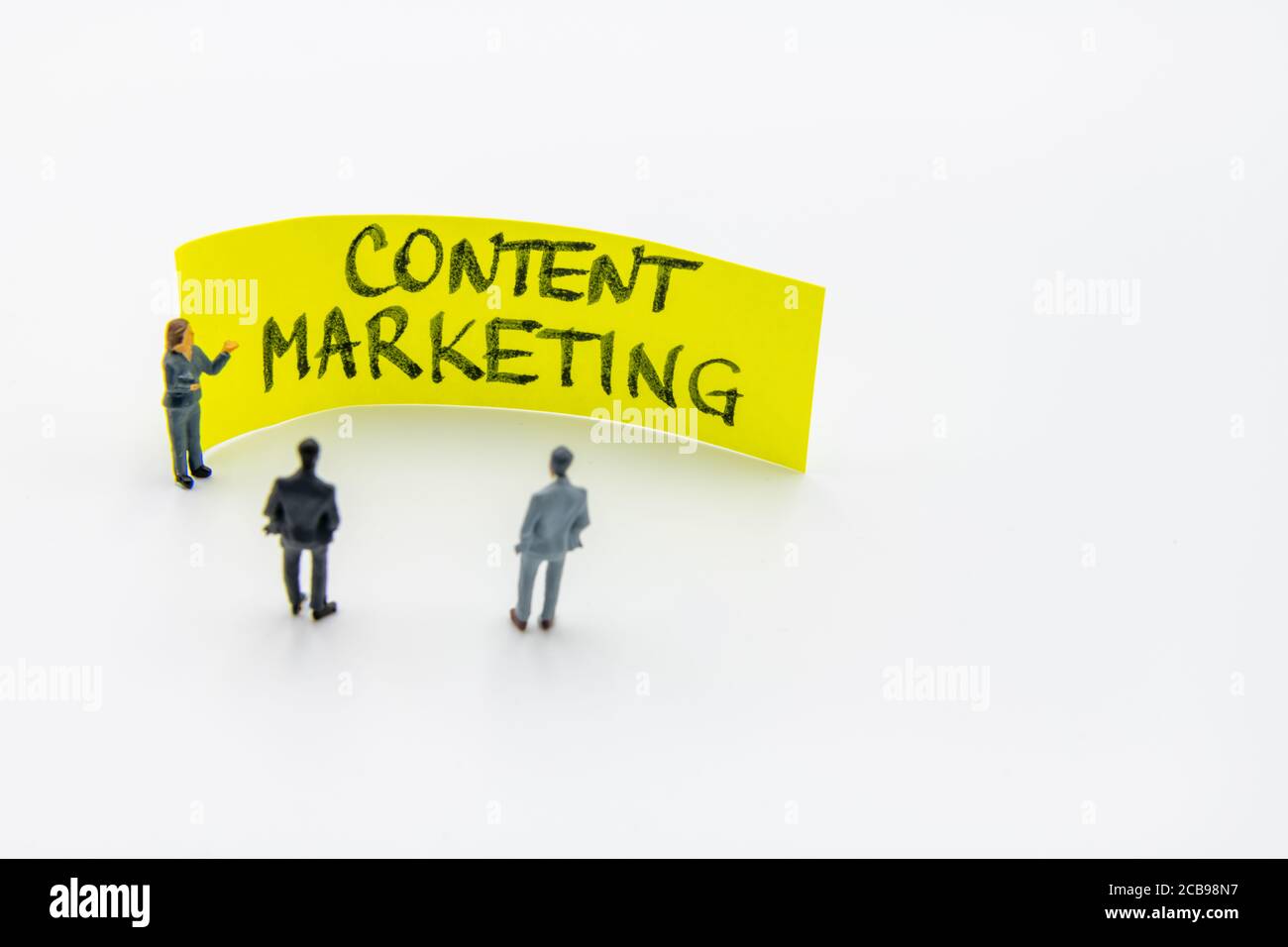 Presentation meeting with miniature figurines posed as business people standing in front of post-it note with Content Marketing handwritten message in Stock Photo