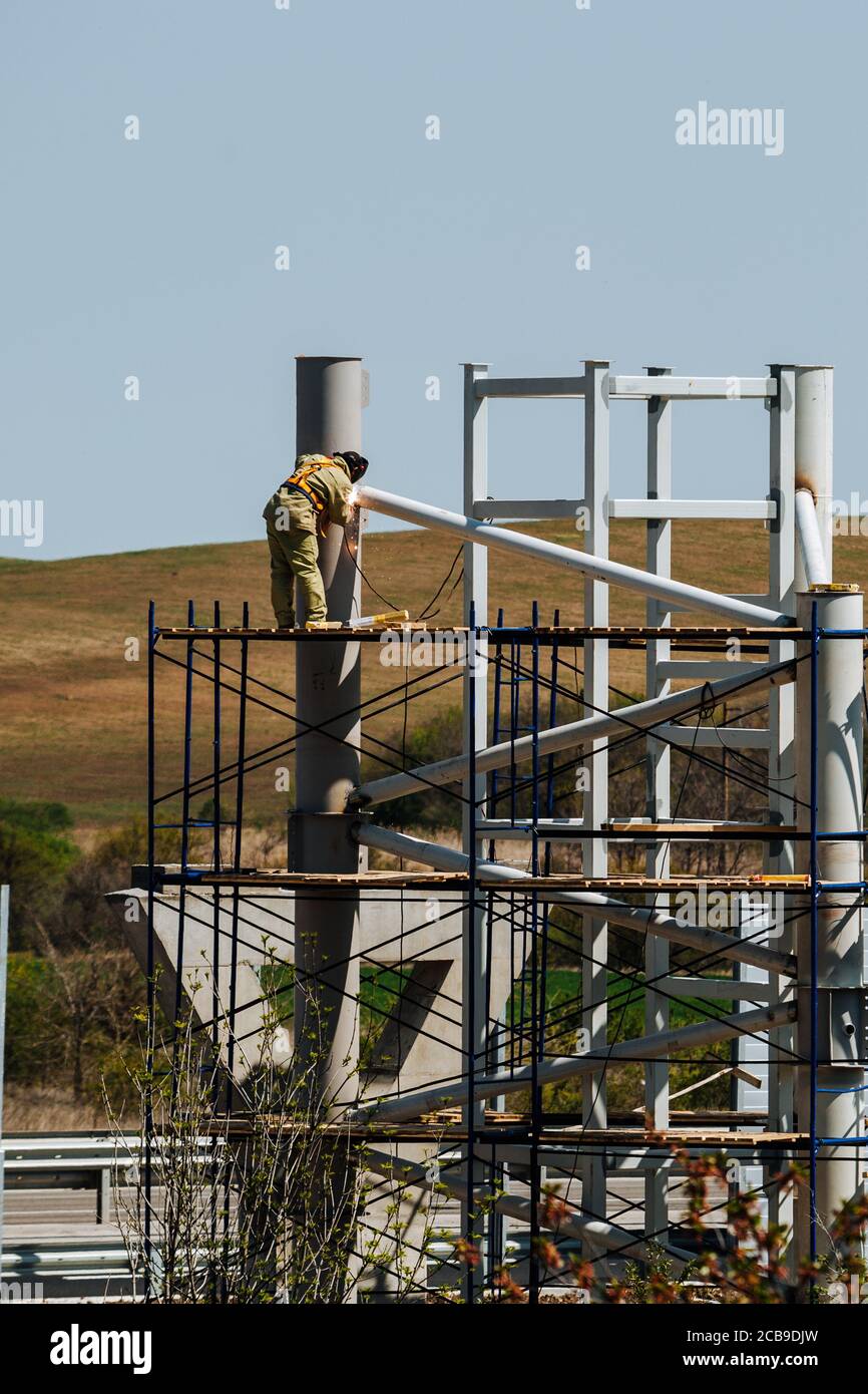 Worker is working at a construction site while on scaffolding. Workers are welding. Metal construction. Stock Photo