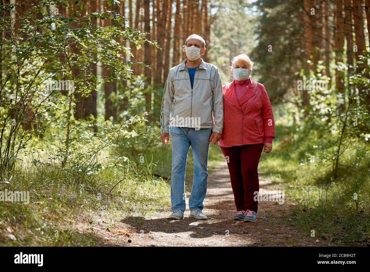 an elderly couple in protective masks walking in the Park, a walk in the fresh air after quarantine, a precaution against the virus Stock Photo