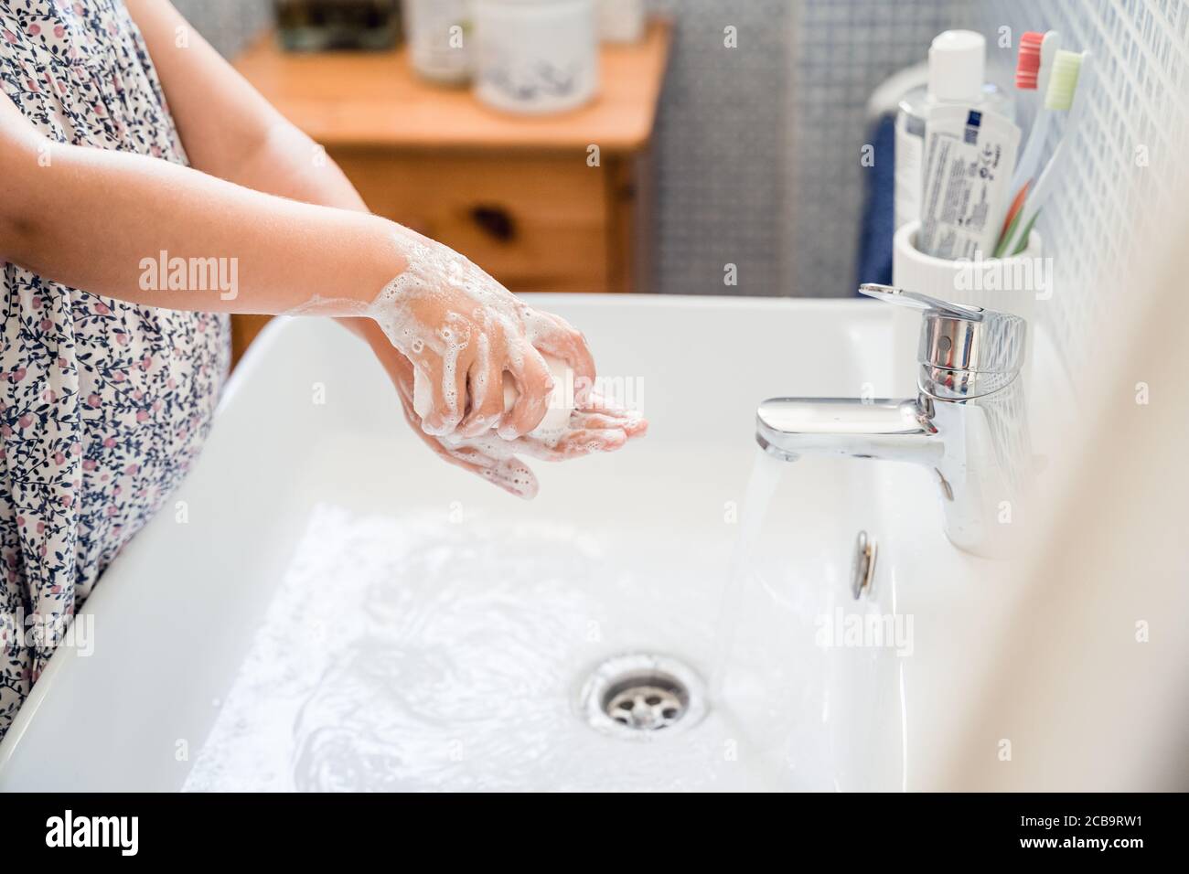 Little girl washes hands with bar of soap in washbasin under running tap water Stock Photo