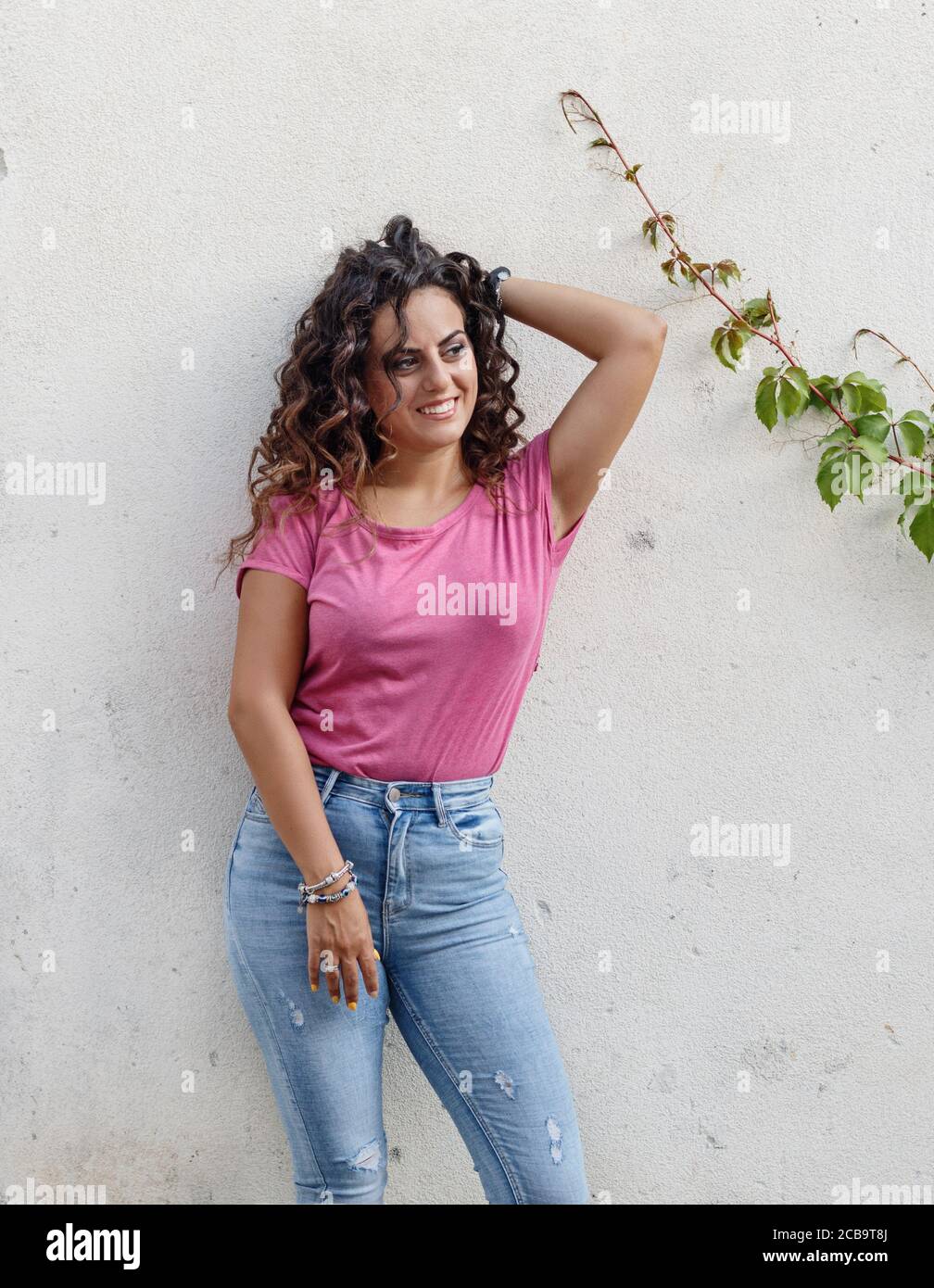 Young women wearing t-shirt and jeans stays near a wall and smile Stock Photo