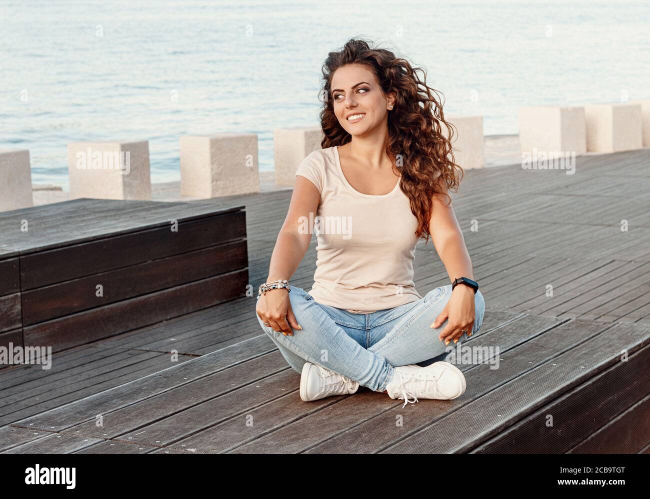 Young women wearing t-shirt and jeans sits on the wooden bench and smile  Stock Photo - Alamy