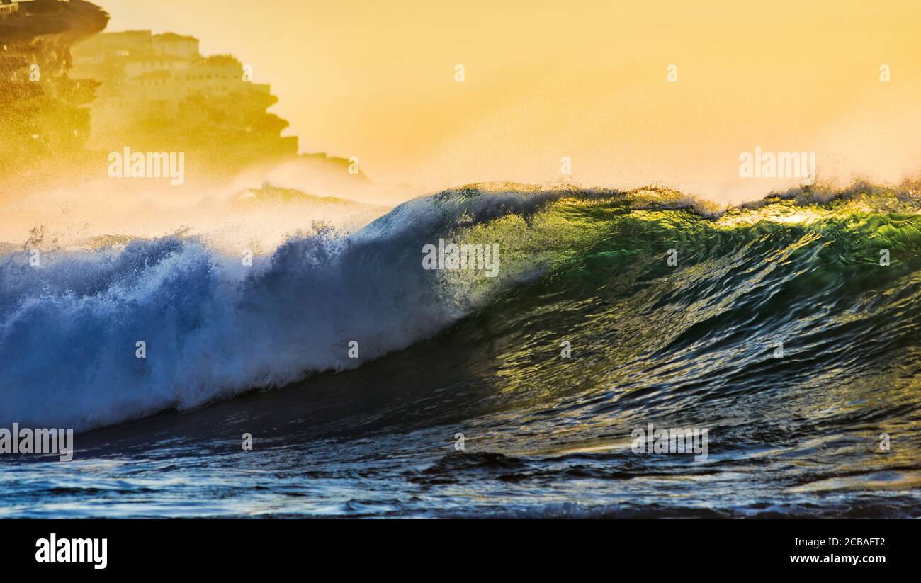 Emerald wave rolling at Bronte beach in Sydney Eastern suburb of Pacific coast at sunrise around sandstone cliffs. Stock Photo
