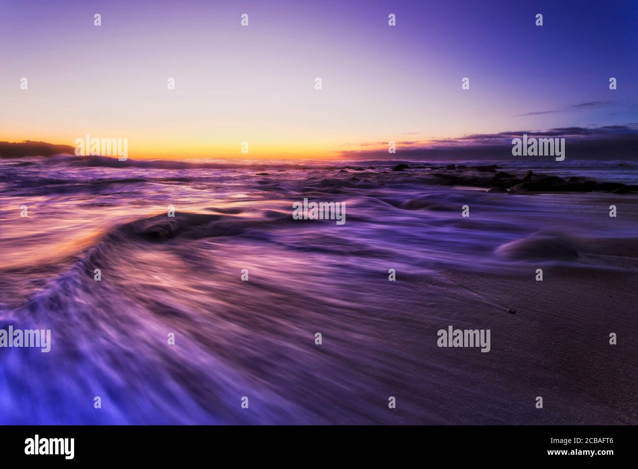 Tail of outgoing wave on sands of Bronte beach in Sydney at dawn facing risign sun and Pacific ocean. Stock Photo