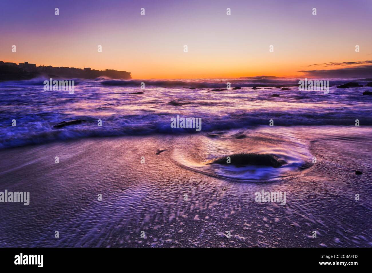Sandy Bronte beach on Sydney Eastern suburbs coast of Pacific ocean at sunrise pre dawn with blurred water waves around rocks. Stock Photo
