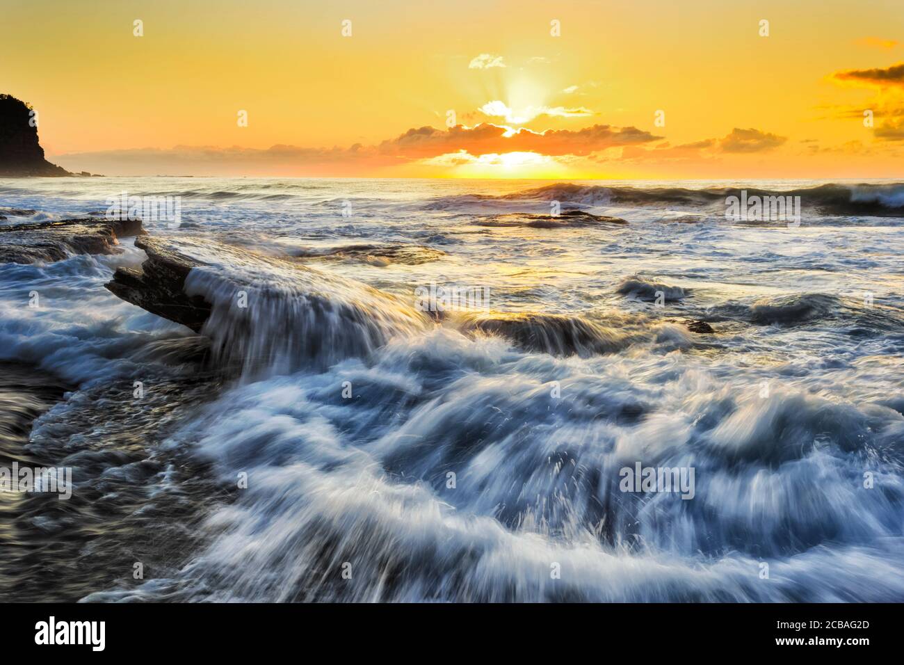 Sun over Pacific ocean horizon at Bungan beach of Sydney Northern beaches at sunrise with strong waves. Stock Photo