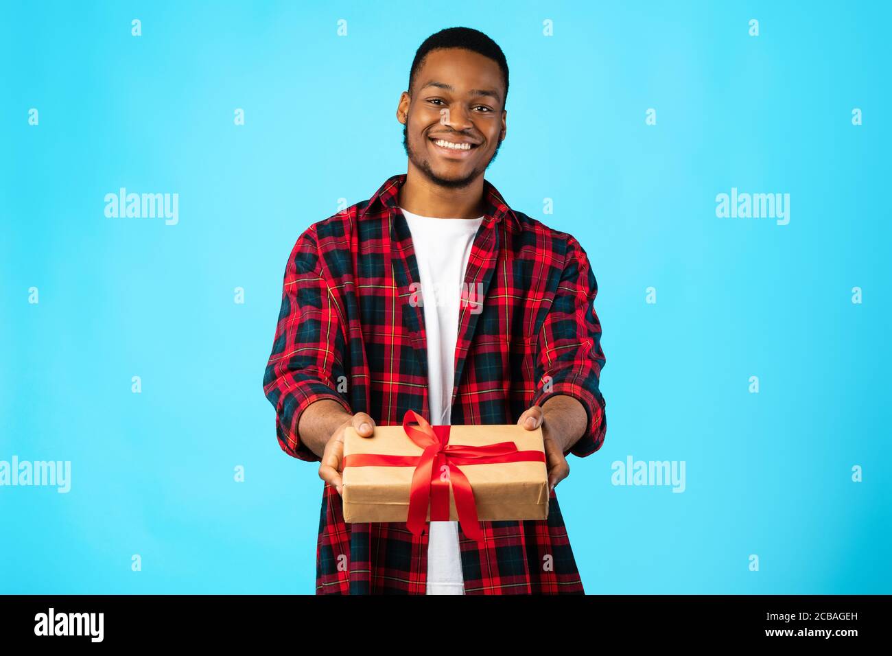 Cheerful African Guy Giving Gift To Camera Posing In Studio Stock Photo