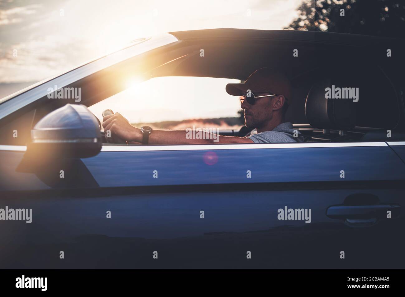 Caucasian Men in His 40s in Baseball Hat and Sunglasses Enjoying Drive His Modern Convertible Car. Driving Cabriolet Theme. Midlife Crisis Concept. Stock Photo