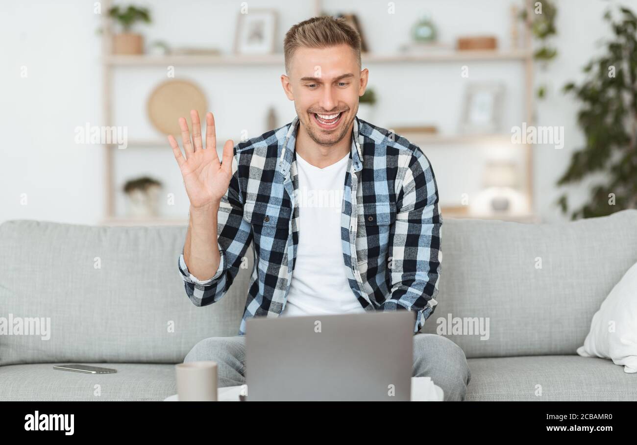 Happy guy using computer for video call and waving Stock Photo - Alamy