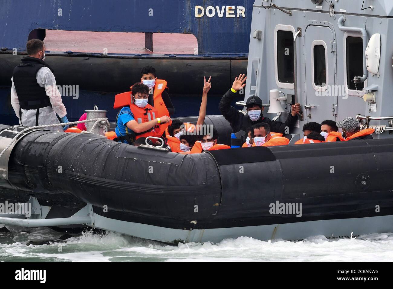 A group of people thought to be migrants, one is waving, are brought into Dover, Kent, by Border Force officers following a number of small boat incidents in the Channel earlier today. Stock Photo