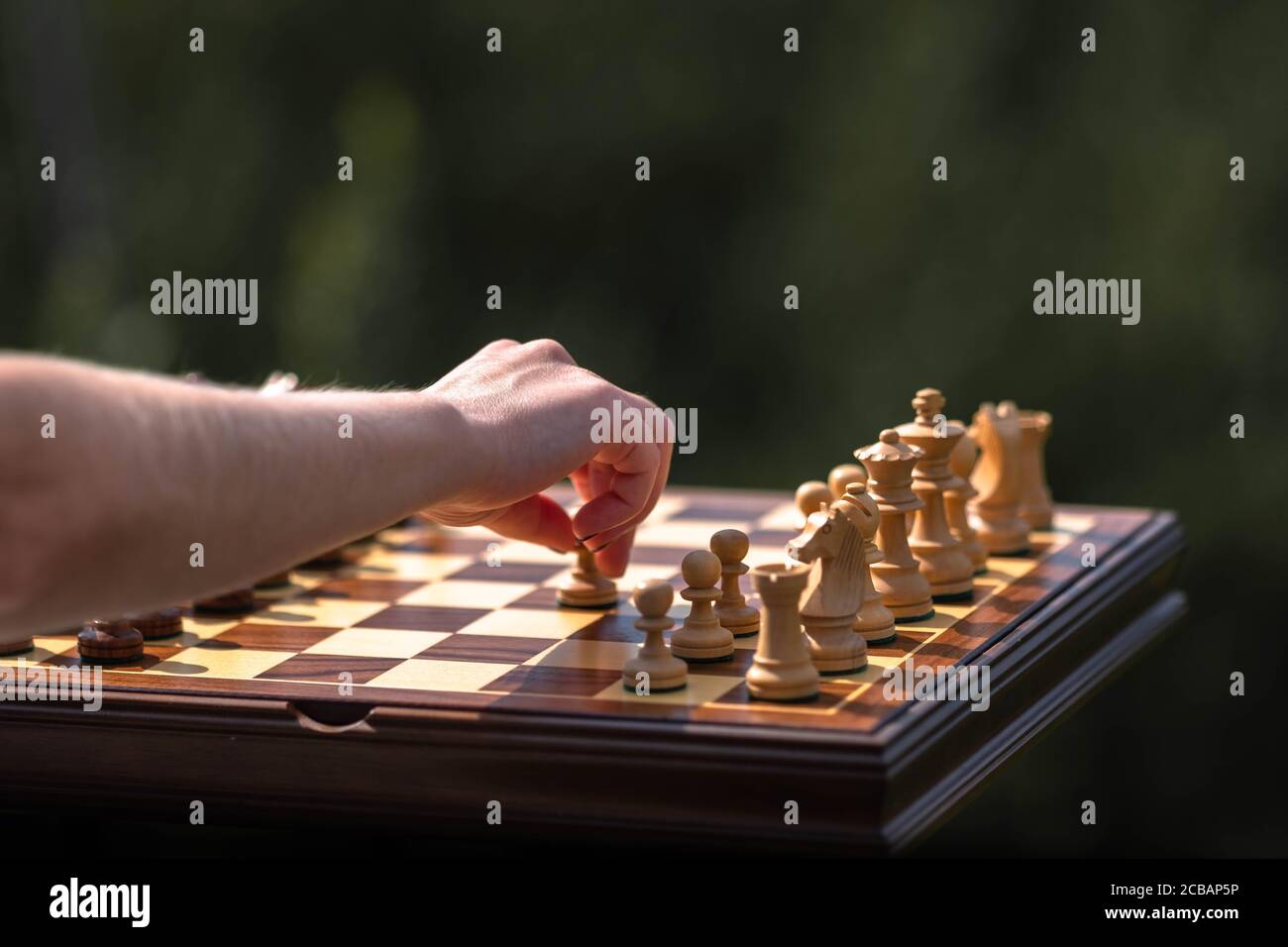 Female hand moves pawn on chessboard with set pieces. Wooden Chessboard