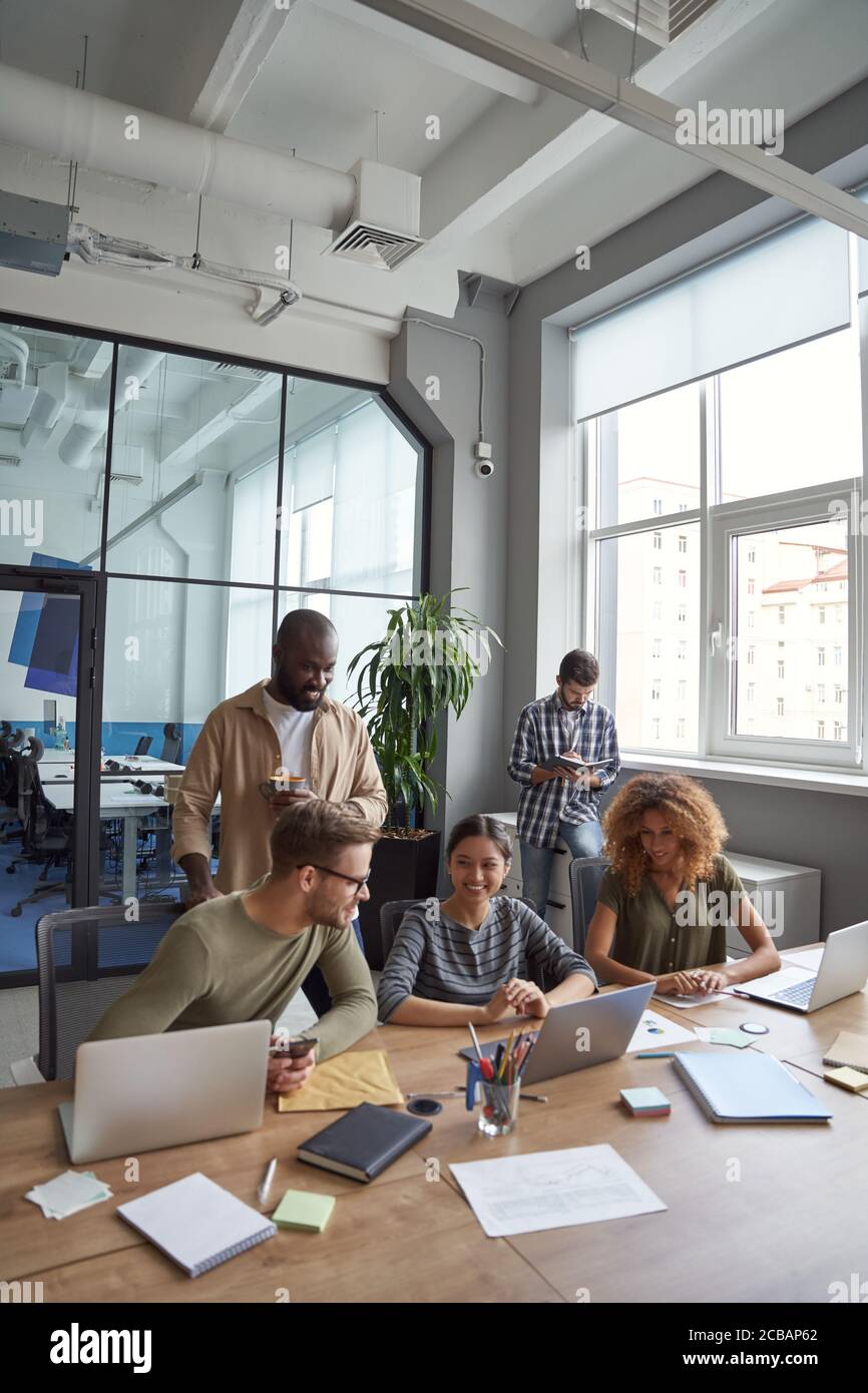 Successful team in coworking space. Vertical shot of multiracial coworkers communicating, sharing fresh ideas while working together in the modern Stock Photo