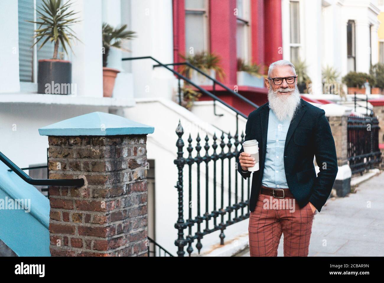 Senior hipster man going out from home while drinking coffee at morning time - Trendy lifestyle,  and joyful elderly lifestyle concept - Focus on face Stock Photo