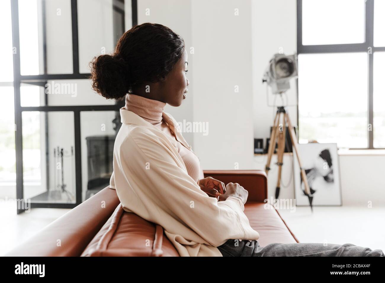 Attractive young smiling african woman sitting on a couch at home ...
