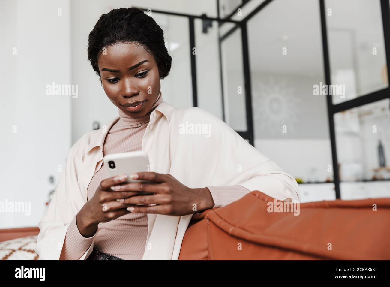 Image of serious young african woman sitting on sofa indoors at home ...