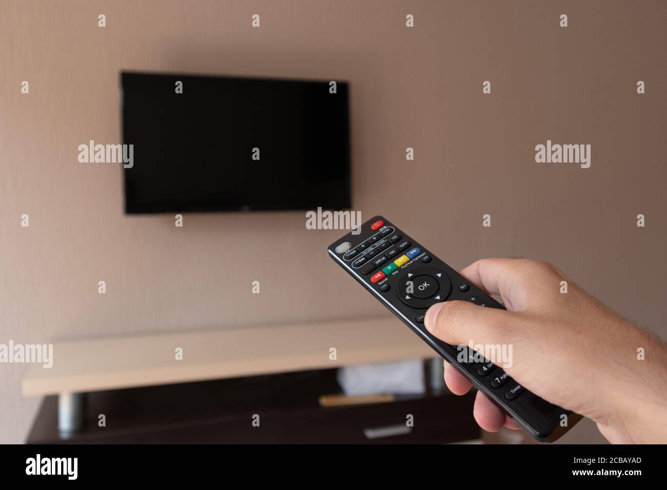 Male hand with tv remote control and blurred television with a black ...