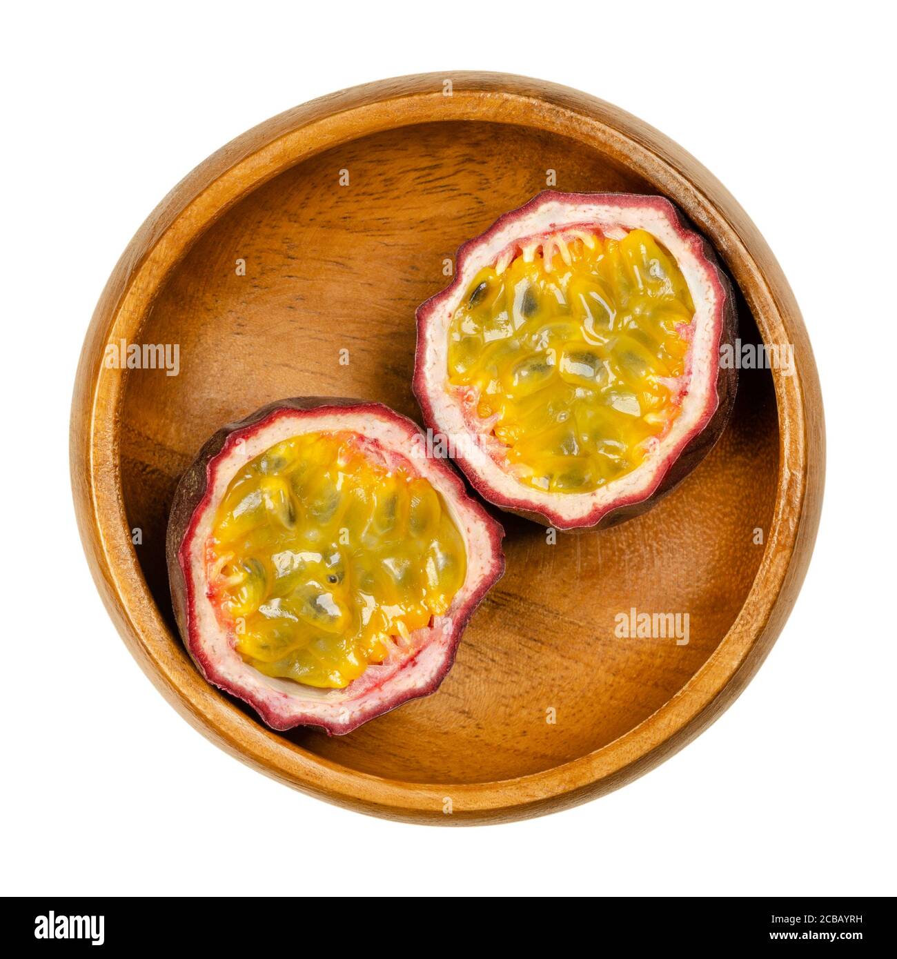 Fresh passion fruit cut in two halves, in wooden bowl. Fruits with purple skin and yellow flesh with many seeds. Can be eaten raw. Stock Photo