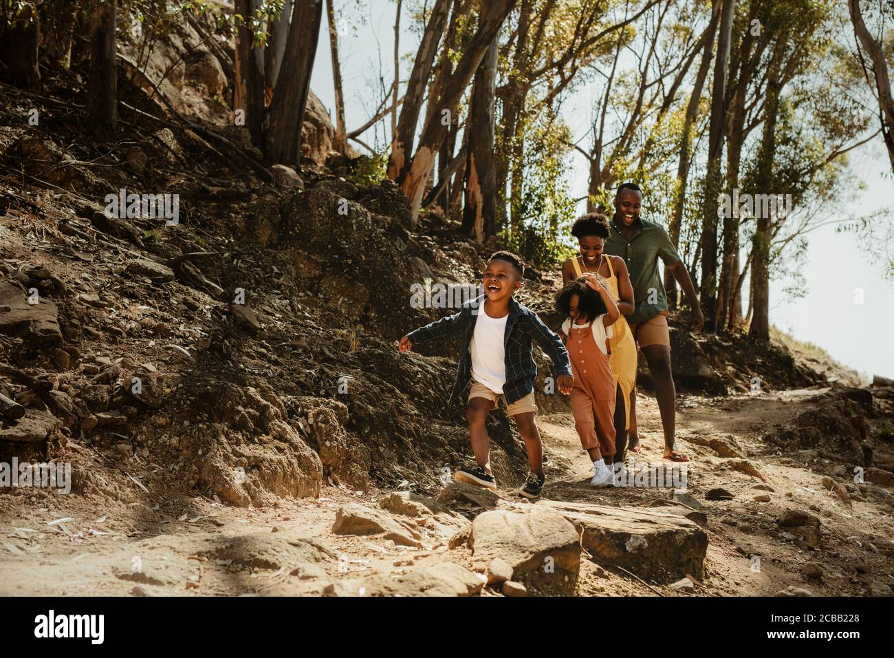 Young family running down rocky mountain trail. Two kids running with parent on a trail in forest. Stock Photo