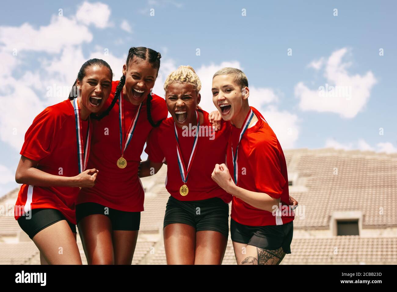 Female football team celebrating the victory at stadium. Woman soccer players with medals shouting in joy after winning the championship. Stock Photo