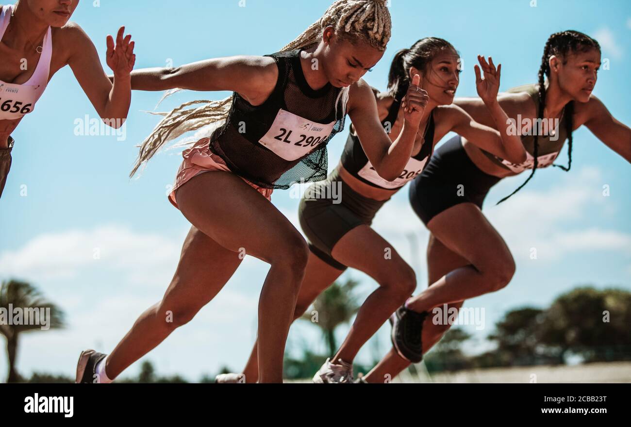 Athletes starting off for a race on a running track. Female runner starting a sprint at stadium track. Stock Photo