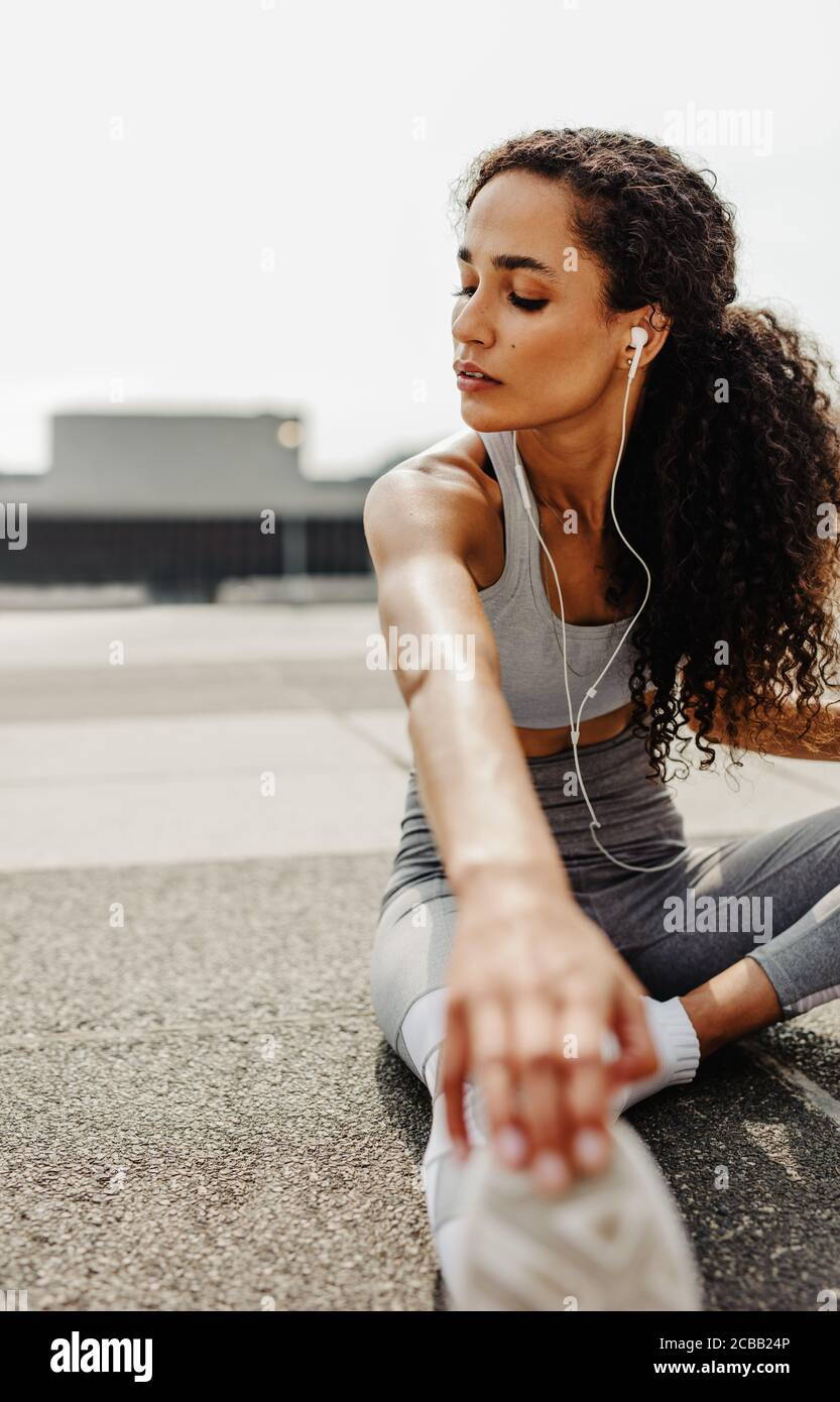 Fitness woman sitting outdoors and stretching. Sporty woman doing some stretching exercises in morning. Stock Photo