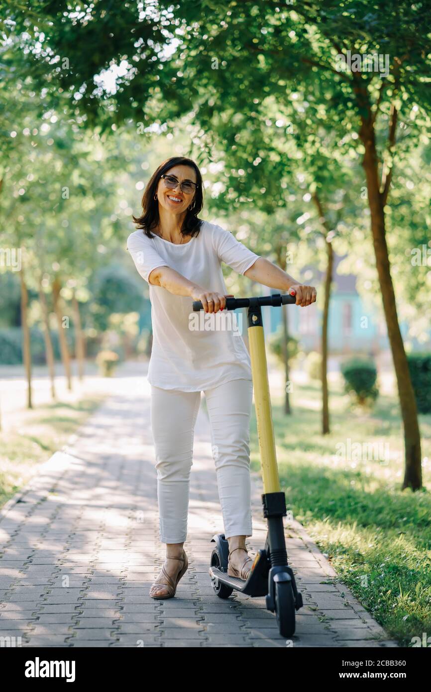 Joyful adorable senior woman using a scooter while riding in the park. Modern woman, a new generation. Healthy cheerful senior retired lady. Concept Stock Photo