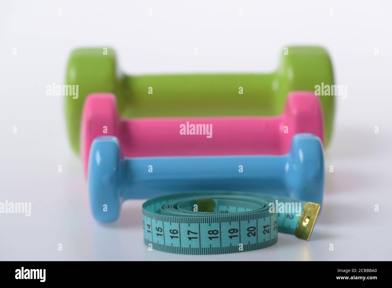 Health regime and fitness symbols. Barbells in small size next to blue measure tape close up. Dumbbells made of blue pink and green plastic on white defocused background. Fit shape and sport