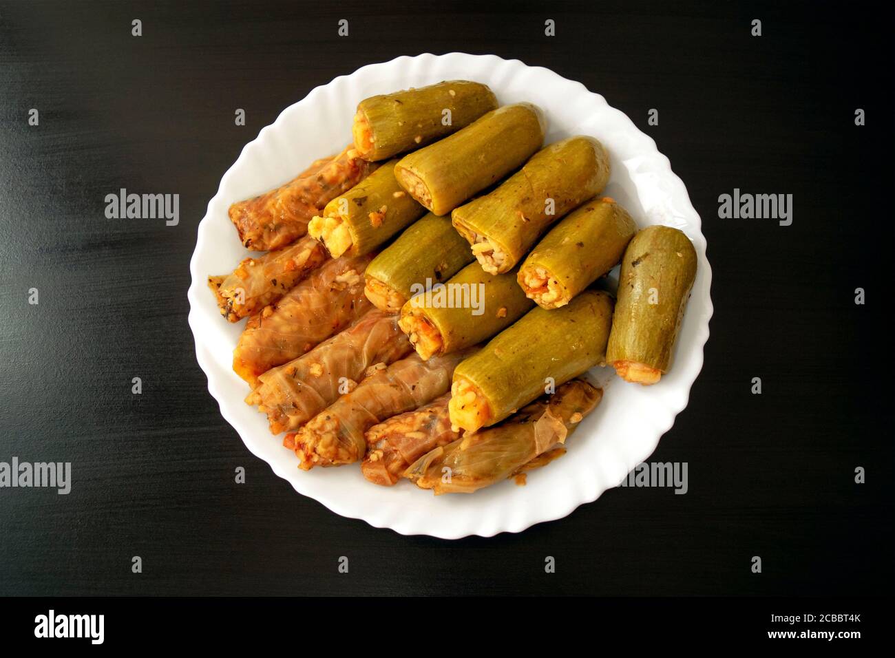Traditional stuffed squash and cabbage rolls on white plate on dark