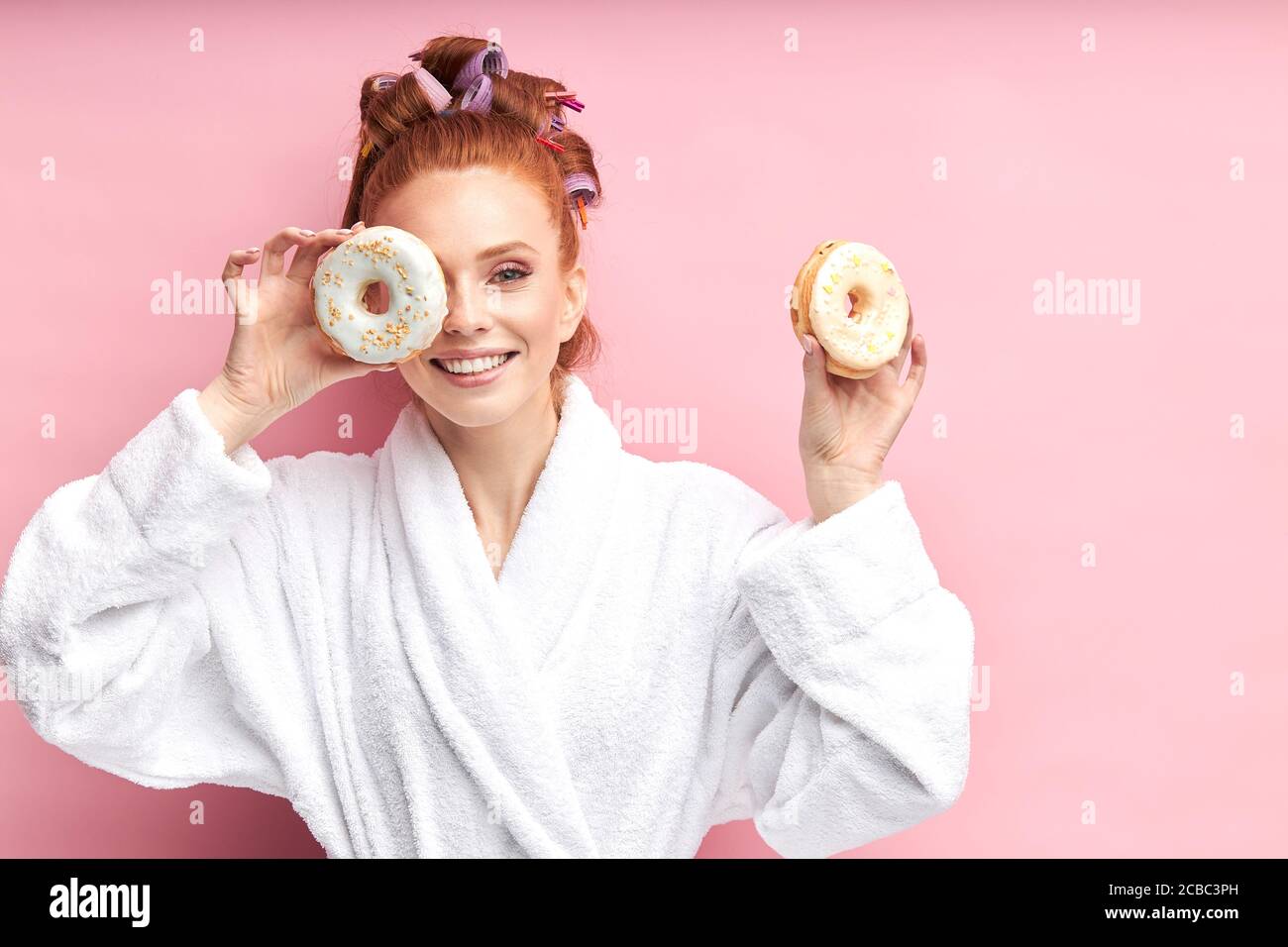 Cute redhead girl with donuts in bathrobe after shower. Portrait of