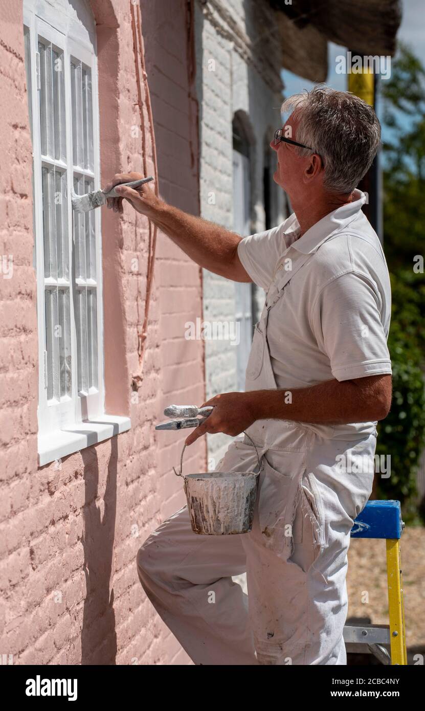 Hampshire, England, UK. 2020. Painter decorator painting small windows on a rural house Stock Photo