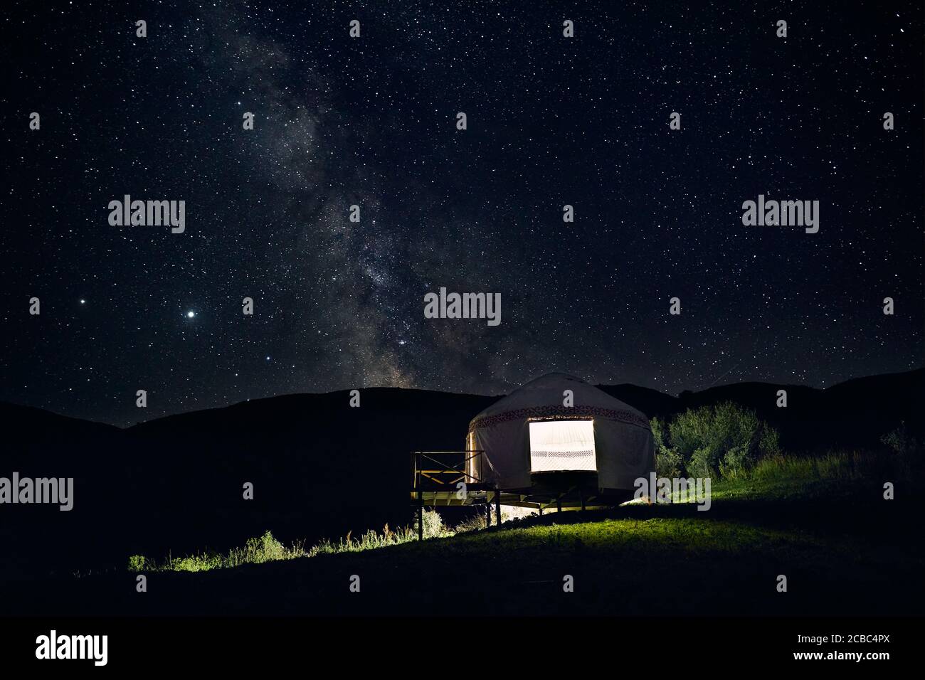 Beautiful gloving Yurt nomadic house at camping in the mountain valley under night sky with stars and Milky Way Stock Photo