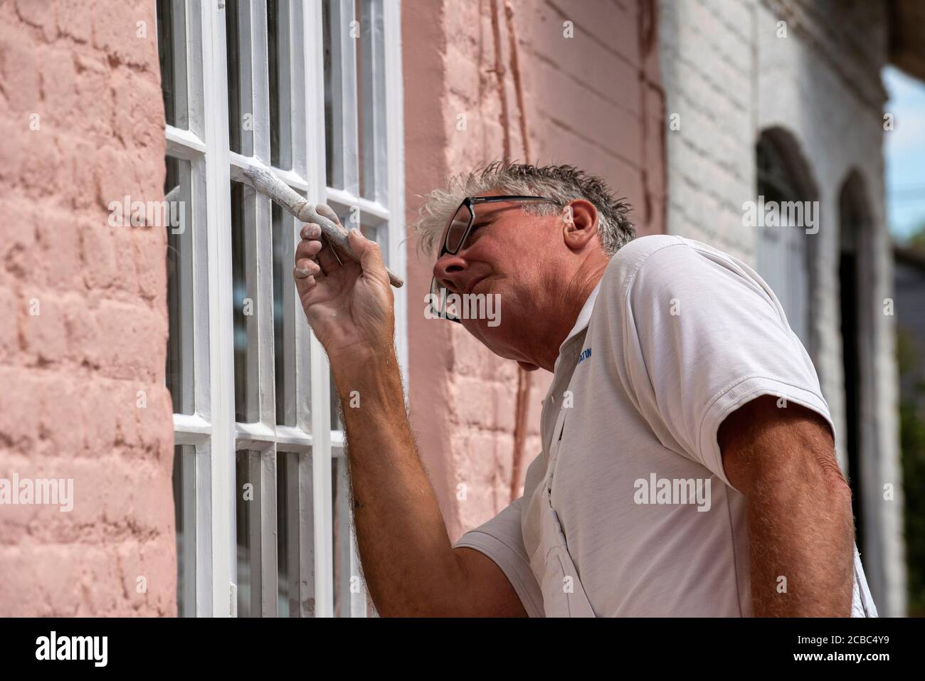 Hampshire, England, UK. 2020. Painter decorator painting small windows on a rural house Stock Photo