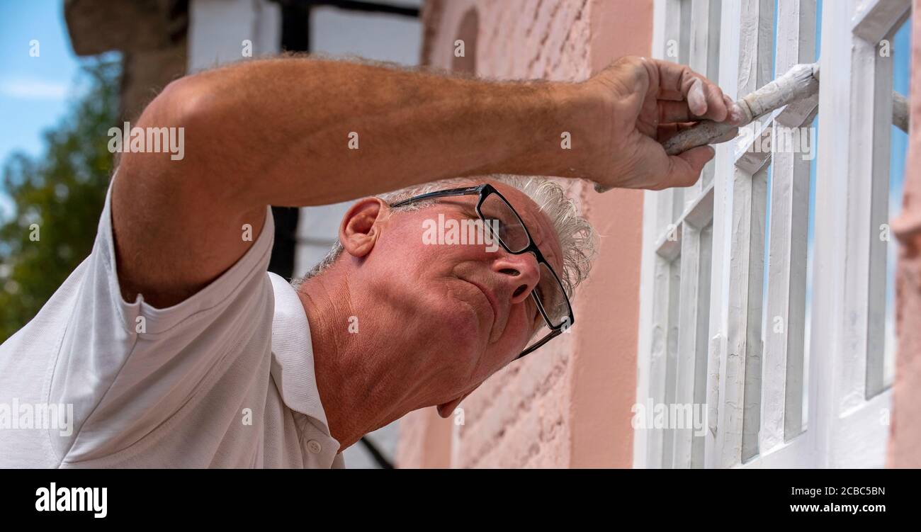 Hampshire, England, UK. 2020. Painter decorator painting small windows on a rural house Stock Photo
