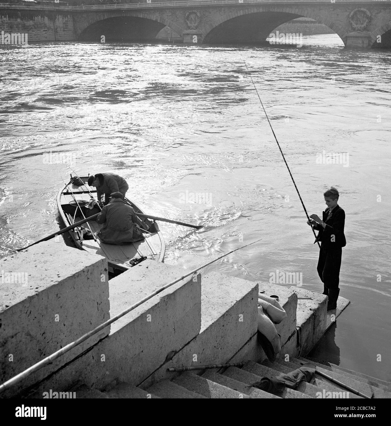 https://c8.alamy.com/comp/2CBC7A2/1950s-historical-paris-france-boy-with-fishing-rod-on-some-steps-down-by-the-river-seine-a-rowing-boat-with-two-men-and-a-fishing-net-sets-off-2CBC7A2.jpg