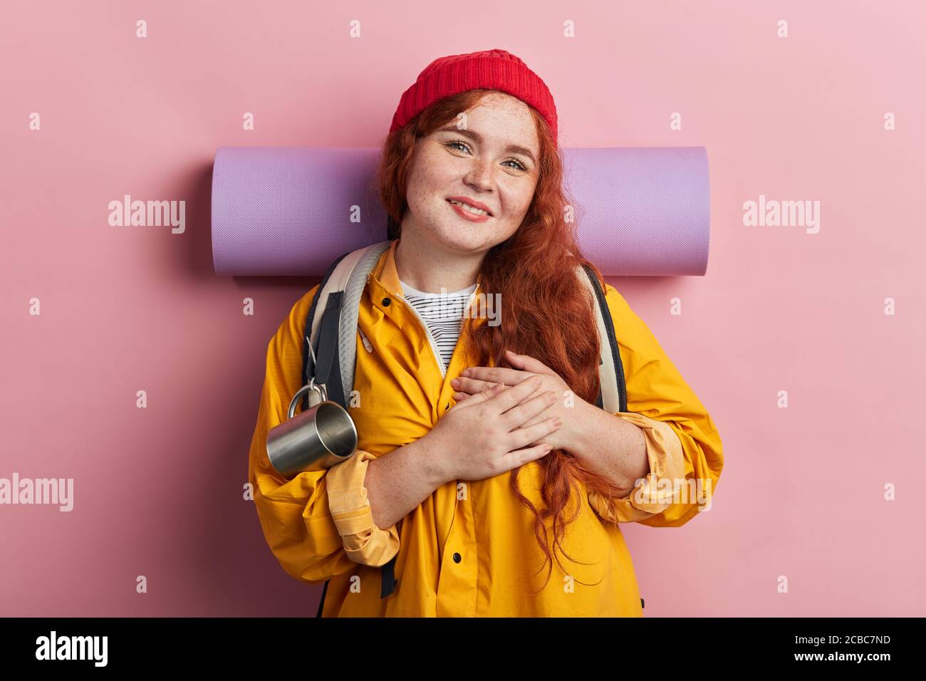 woman wearing rucksack, backpack, yellow coat, green shirt and red knitted  cap has friendly expression, pressing palm to chest. Love concept.thank you  Stock Photo - Alamy