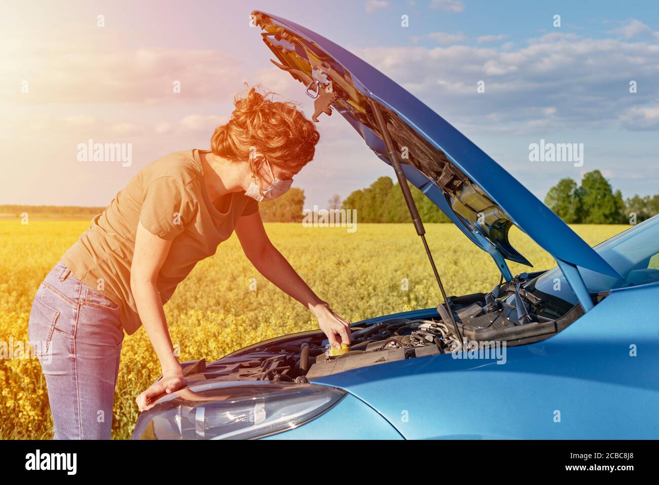 Woman repairs broken car with open hood on the road in summer day Stock
