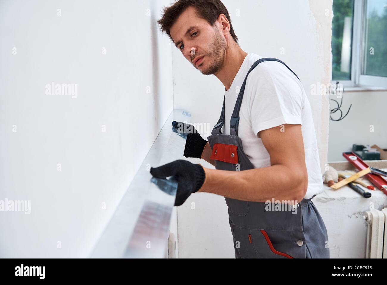 Male worker plastering a wall using a long spatula. Renovation concept Stock Photo