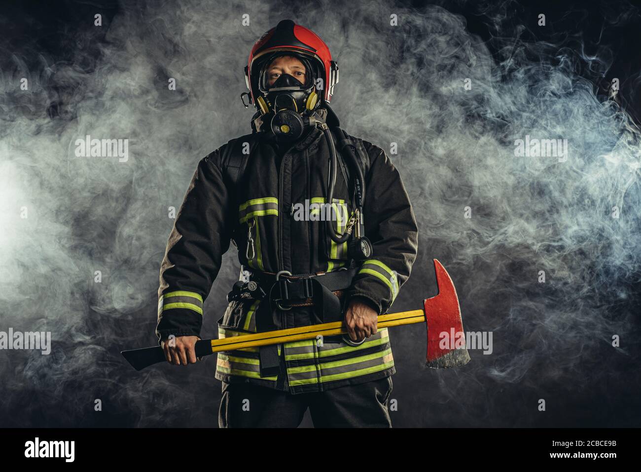 young firefighter preparing to save, to extinguish fire and save people if necessary, holding hammer in hands and wearing protective suit uniform Stock Photo