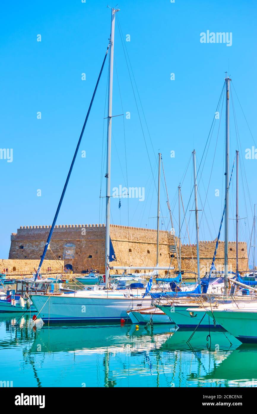 Marina in Heraklion. Sailing yachts with tall masts in the harbour by the Venetian Fortress on sunny summer day, Crete island, Greece Stock Photo