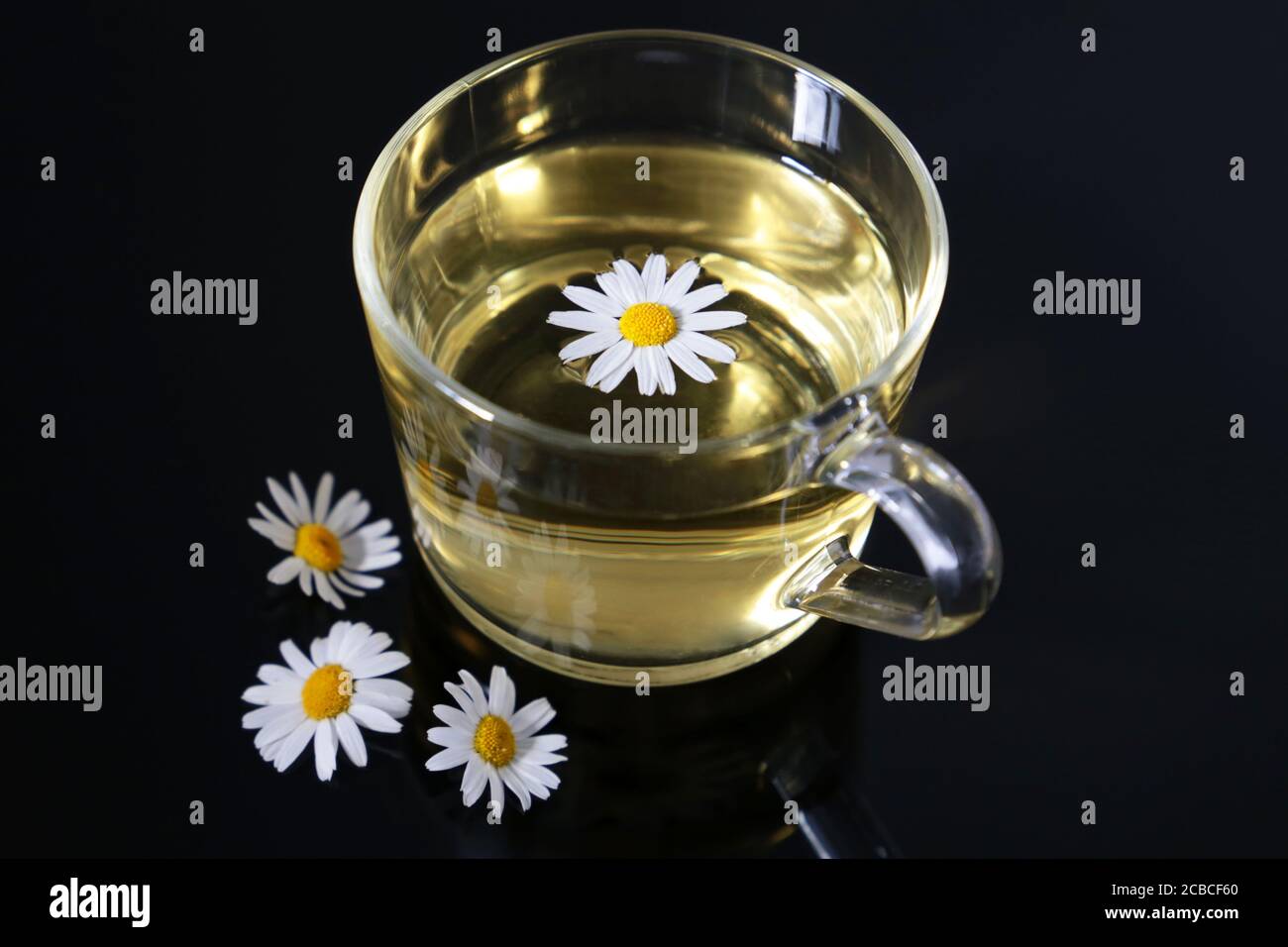 Chamomile tea in a transparent glass cup and daisy flowers on dark ...