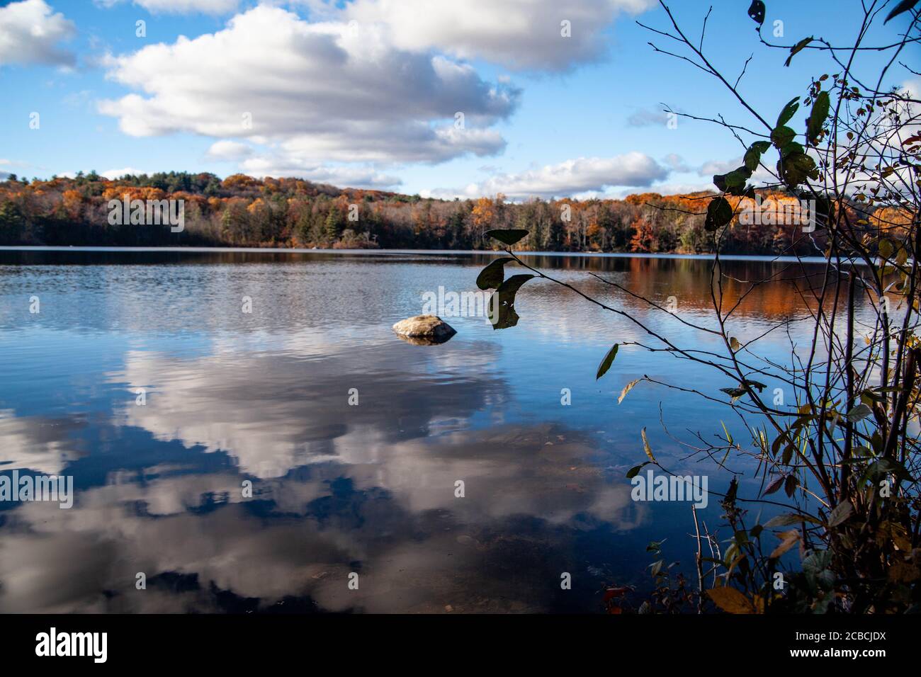 The rippled water of the lake reflects the blue sky and white clouds and the autumn forest is visible in the distance during a sunny bright day Stock Photo