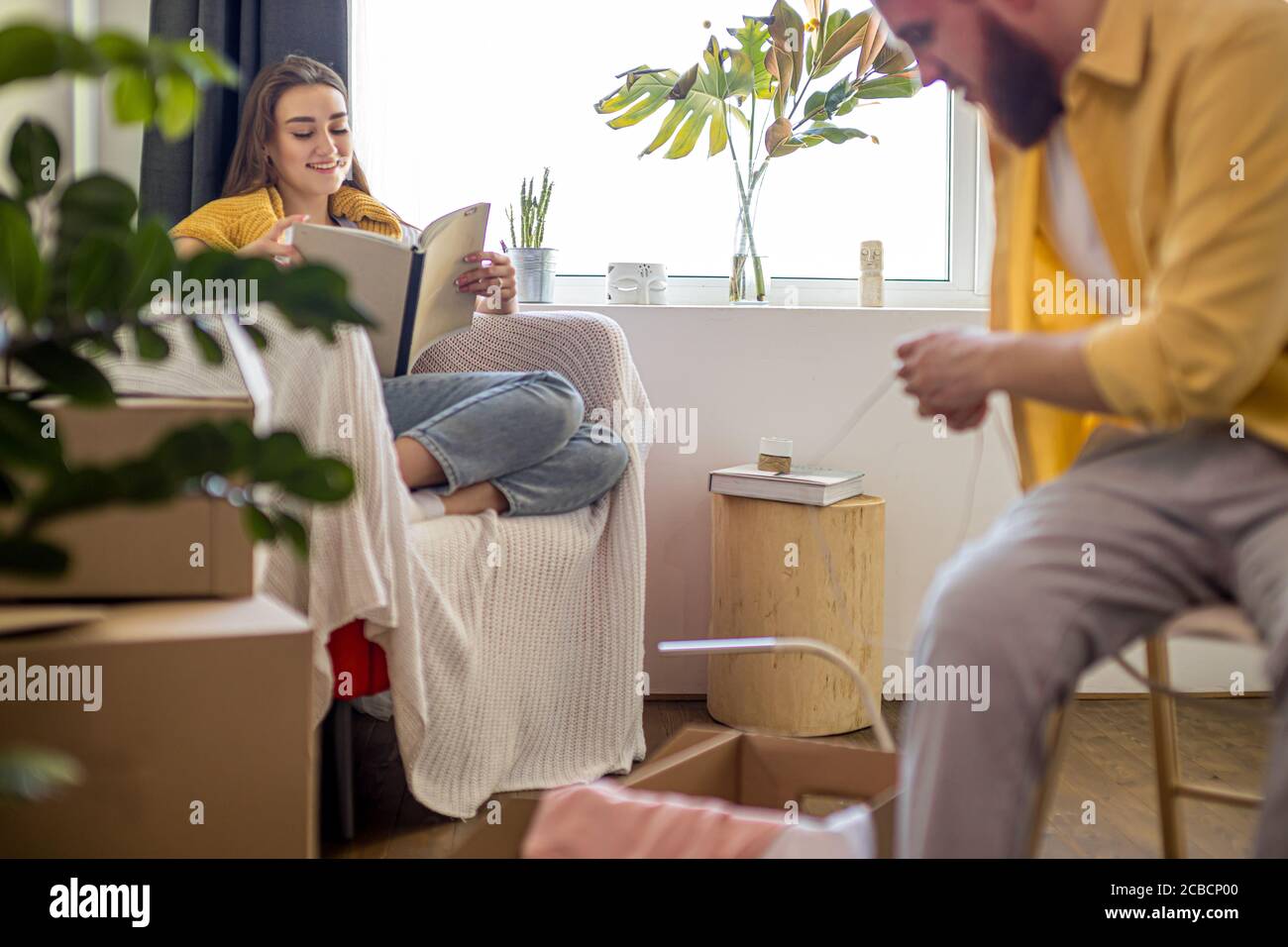 man unpacking cardboard boxes after moving into new house, tired woman have rest, read a book. indoors Stock Photo