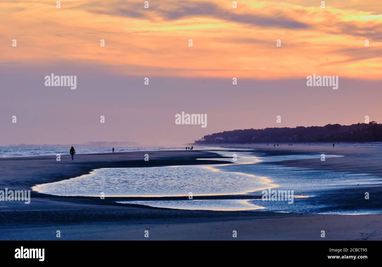 A few people enjoy a quiet beach stroll on Hilton Island during a muted, winter sunset Stock Photo